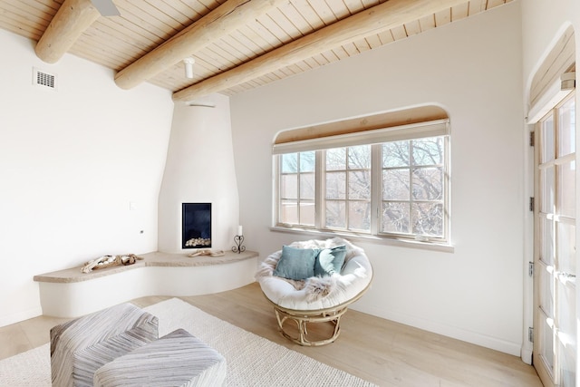 sitting room featuring beamed ceiling, light wood-type flooring, a fireplace, and wood ceiling