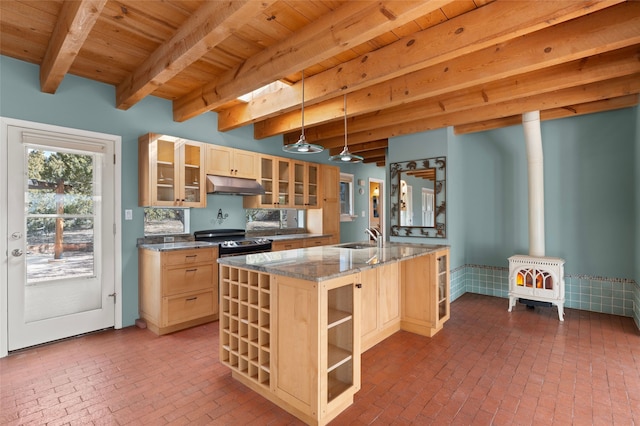 kitchen featuring sink, dark stone countertops, hanging light fixtures, light brown cabinetry, and a wood stove