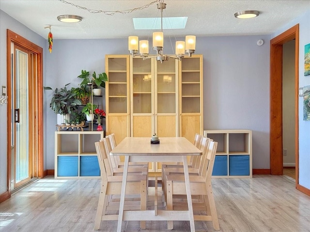 dining area with wood-type flooring, a chandelier, a textured ceiling, and a skylight