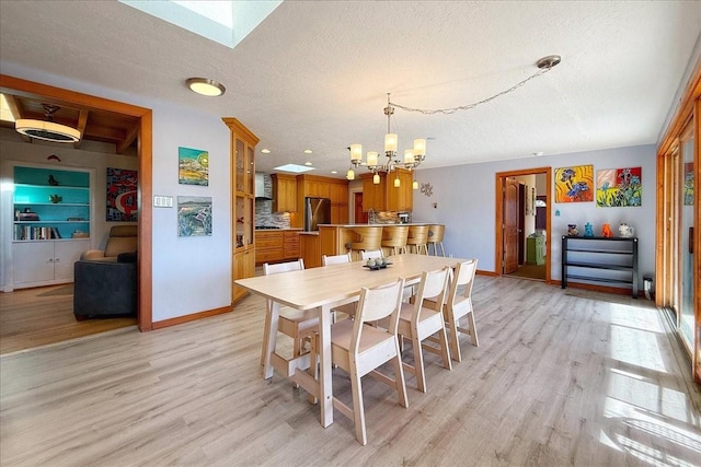 dining room featuring a skylight, an inviting chandelier, a textured ceiling, and light hardwood / wood-style flooring