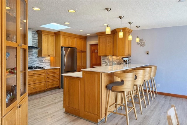 kitchen featuring hanging light fixtures, kitchen peninsula, stainless steel appliances, light hardwood / wood-style floors, and backsplash