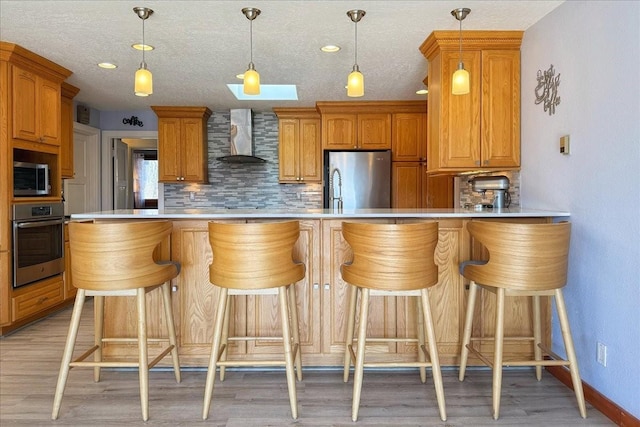 kitchen featuring a kitchen breakfast bar, decorative backsplash, kitchen peninsula, stainless steel appliances, and wall chimney exhaust hood