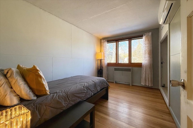 bedroom featuring vaulted ceiling, radiator, a wall mounted air conditioner, and light wood-type flooring