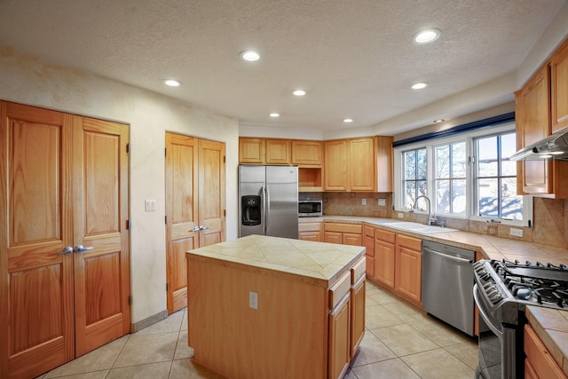 kitchen with sink, tile countertops, a kitchen island, stainless steel appliances, and backsplash