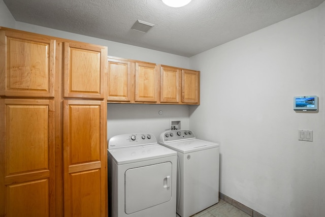 clothes washing area featuring washing machine and dryer, cabinets, a textured ceiling, and light tile patterned flooring