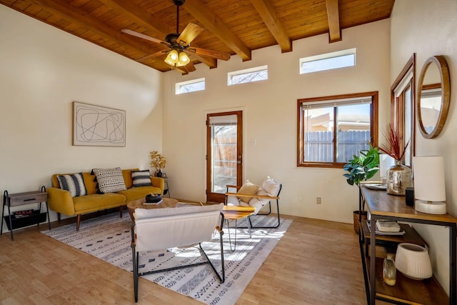 living room with beamed ceiling, a high ceiling, ceiling fan, wooden ceiling, and light wood-type flooring