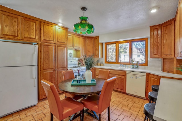 kitchen featuring sink, hanging light fixtures, a textured ceiling, white appliances, and decorative backsplash