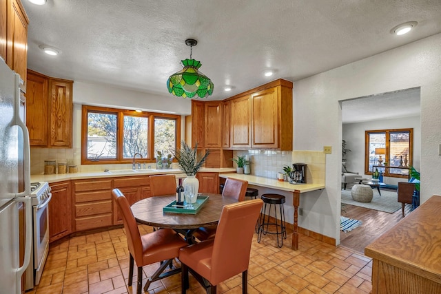 kitchen with sink, white appliances, hanging light fixtures, and backsplash