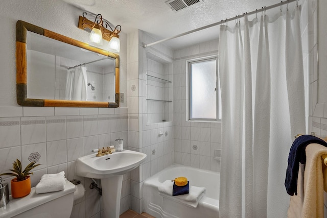 full bathroom featuring sink, tile walls, shower / tub combo, toilet, and a textured ceiling