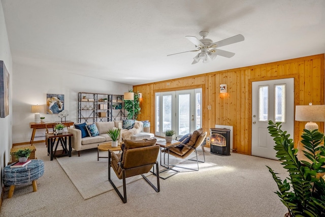 living room with ceiling fan, light colored carpet, wood walls, and a wood stove