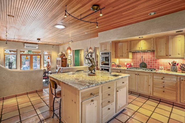 kitchen featuring decorative backsplash, sink, a center island with sink, and light brown cabinets