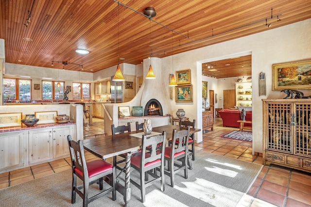 tiled dining area featuring a fireplace, rail lighting, and wooden ceiling