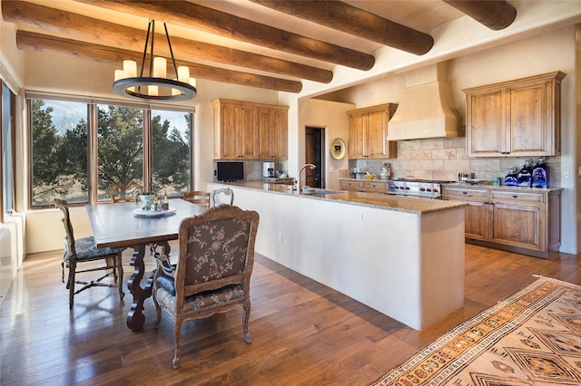 kitchen featuring high end stainless steel range, sink, custom exhaust hood, light stone countertops, and decorative backsplash