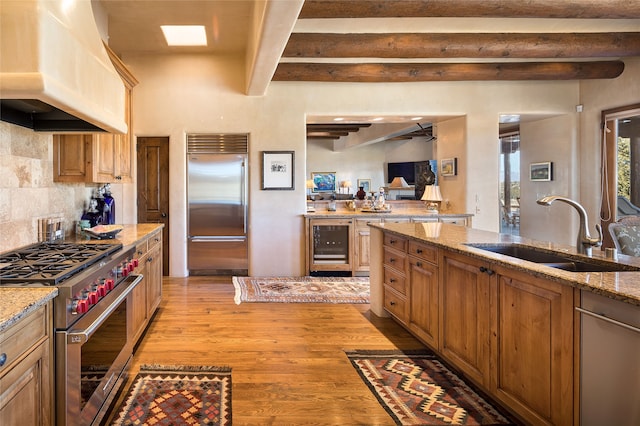 kitchen featuring premium range hood, sink, light stone counters, high quality appliances, and beverage cooler