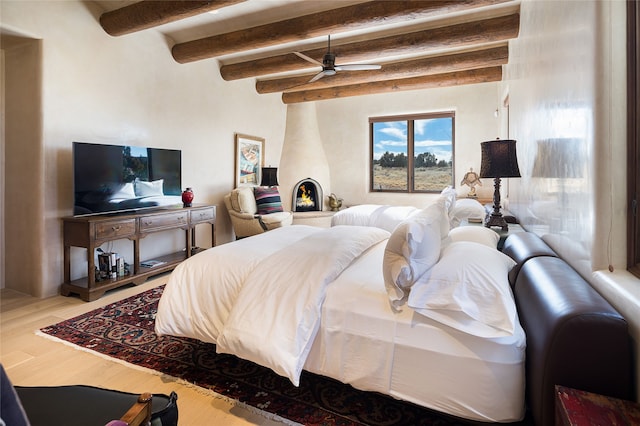 bedroom featuring hardwood / wood-style floors, beam ceiling, and a large fireplace