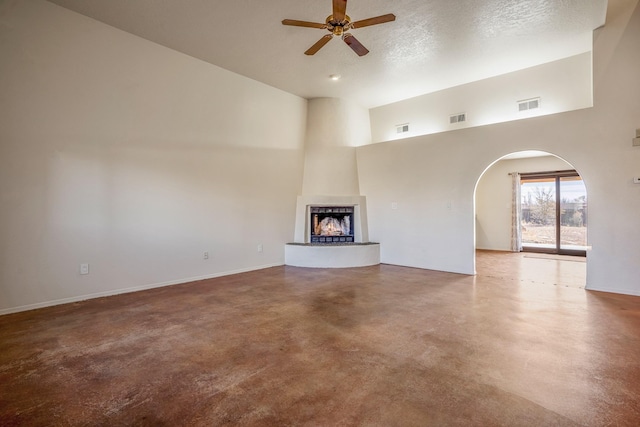 unfurnished living room with concrete flooring, high vaulted ceiling, a textured ceiling, a large fireplace, and ceiling fan