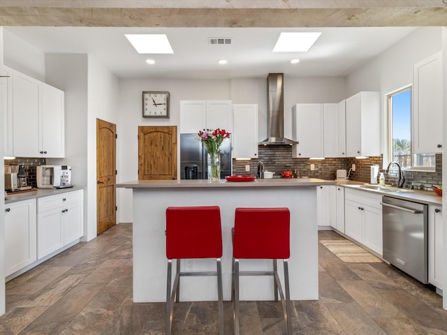 kitchen featuring black fridge, white cabinetry, dishwasher, a kitchen island with sink, and wall chimney range hood