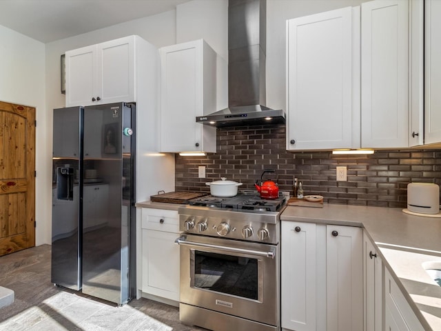 kitchen with high end range, wall chimney range hood, white cabinetry, and refrigerator with ice dispenser