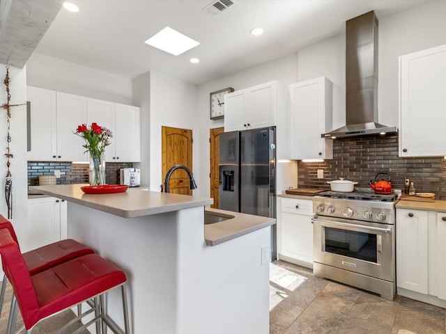 kitchen with stainless steel appliances, white cabinetry, an island with sink, and wall chimney exhaust hood