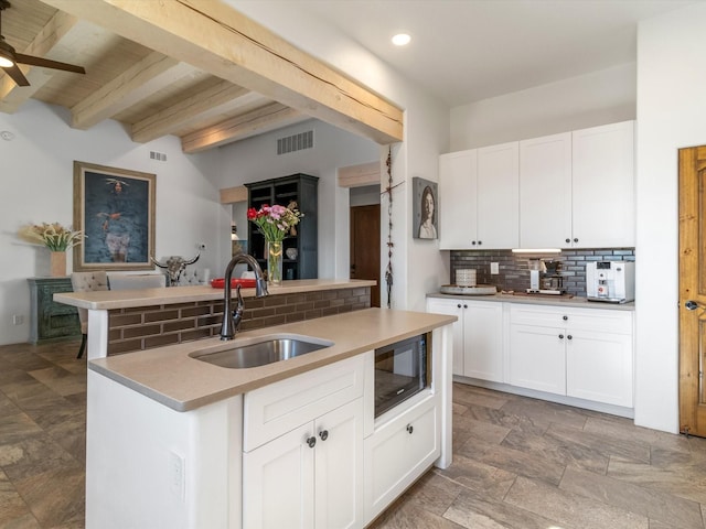 kitchen featuring white cabinetry, sink, decorative backsplash, ceiling fan, and beam ceiling