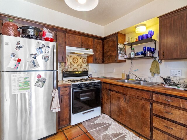 kitchen with pendant lighting, stainless steel refrigerator, backsplash, dark brown cabinetry, and white range with gas cooktop