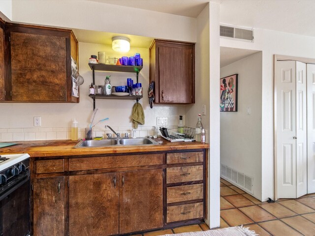 kitchen featuring dark brown cabinetry, butcher block counters, sink, gas stove, and light tile patterned floors