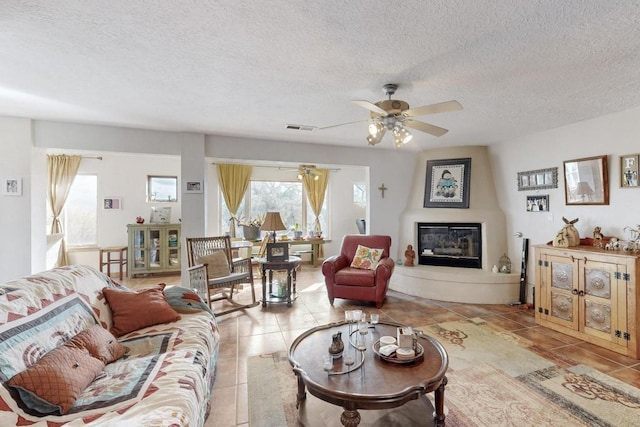 living room featuring visible vents, a textured ceiling, a fireplace, tile patterned flooring, and ceiling fan