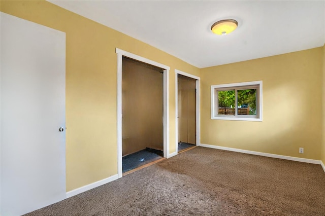 unfurnished bedroom featuring multiple closets and dark colored carpet