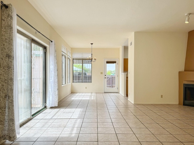 unfurnished living room with a healthy amount of sunlight, light tile patterned floors, a large fireplace, and an inviting chandelier