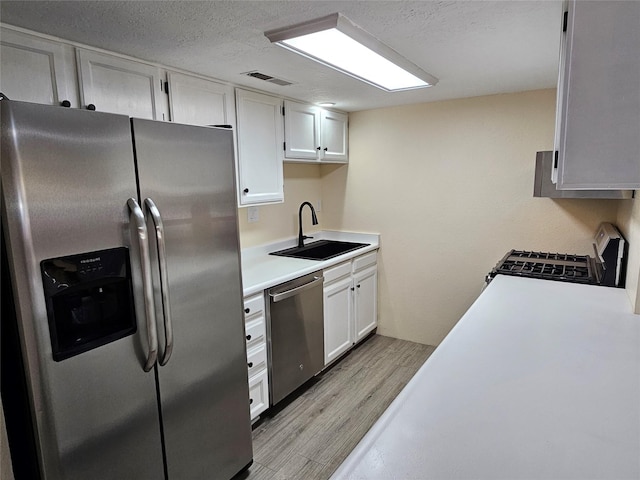 kitchen with sink, a textured ceiling, light wood-type flooring, appliances with stainless steel finishes, and white cabinets