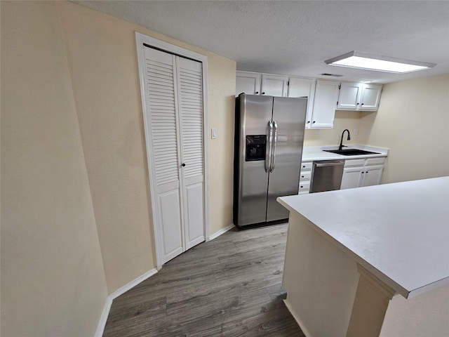 kitchen featuring wood-type flooring, sink, white cabinets, stainless steel appliances, and a textured ceiling