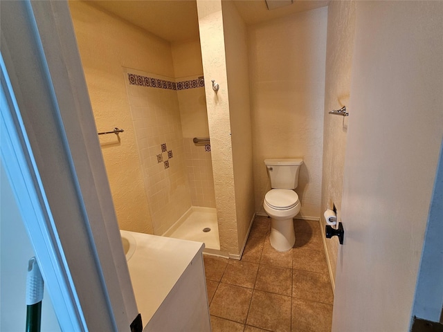 bathroom with tile patterned flooring, toilet, and a tile shower