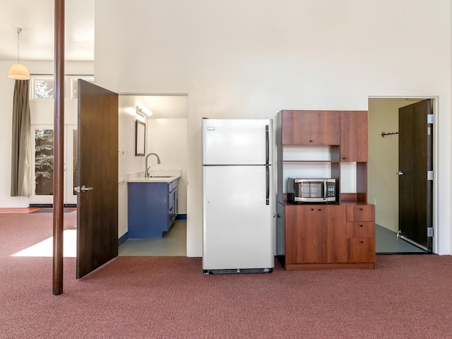 kitchen featuring stainless steel microwave, brown cabinets, freestanding refrigerator, and carpet floors