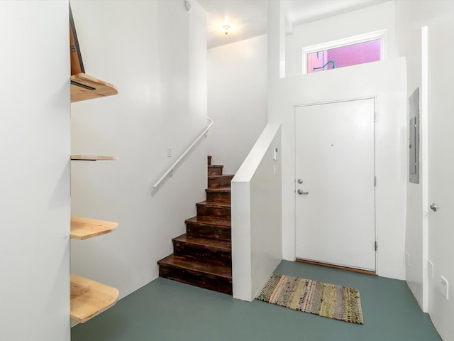 foyer entrance with electric panel, stairway, and finished concrete flooring