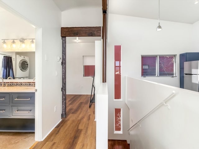 corridor featuring wood finished floors, stacked washer / dryer, and an upstairs landing