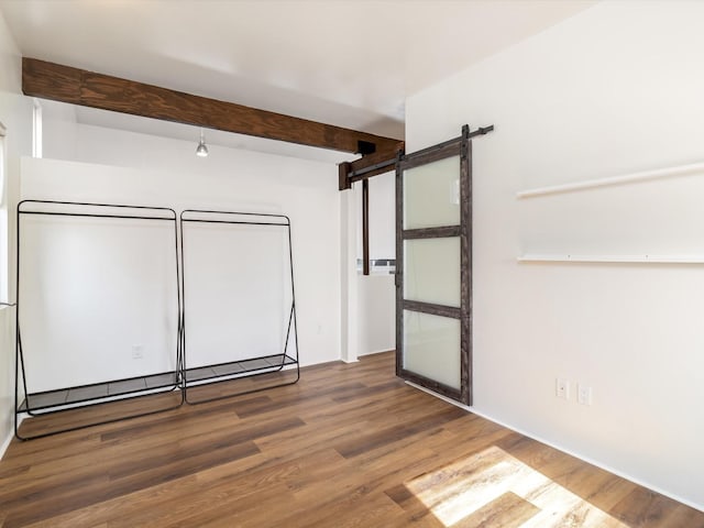 spare room with a barn door, beam ceiling, and wood finished floors