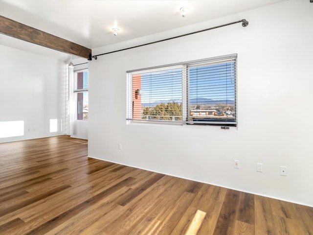 spare room with a wealth of natural light, beam ceiling, and wood finished floors