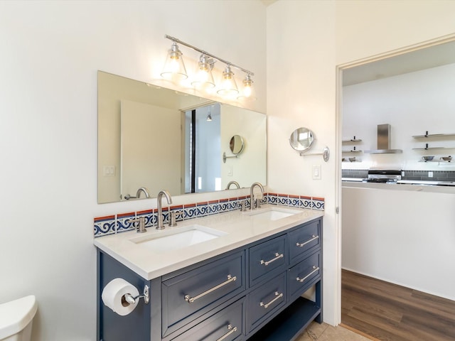 full bath with double vanity, toilet, wood finished floors, and a sink