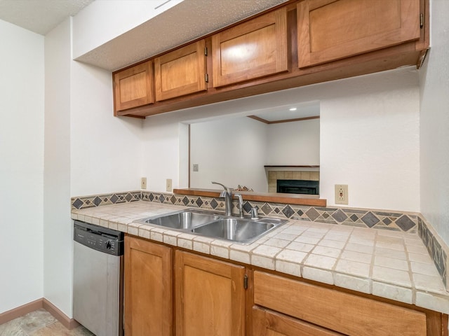 kitchen featuring stainless steel dishwasher, tile countertops, a tiled fireplace, and sink