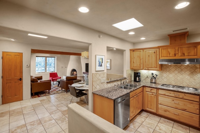 kitchen with appliances with stainless steel finishes, a skylight, sink, backsplash, and light tile patterned floors