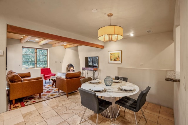 dining space featuring beamed ceiling, a large fireplace, and light tile patterned floors