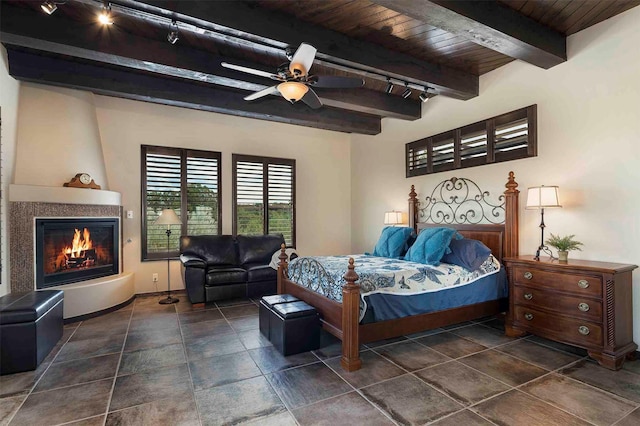 bedroom featuring rail lighting, wood ceiling, beamed ceiling, and a glass covered fireplace