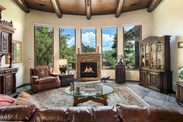 interior space with wood ceiling, a stone fireplace, a wealth of natural light, and beamed ceiling