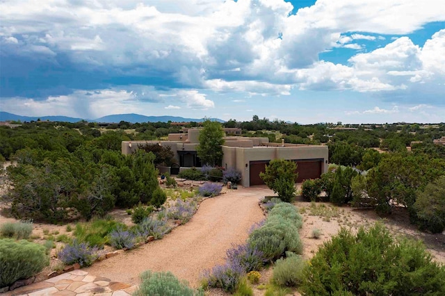 pueblo-style home with a mountain view, an attached garage, dirt driveway, and stucco siding