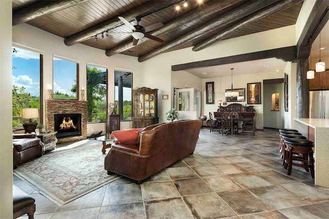 living room featuring wooden ceiling, a ceiling fan, an outdoor stone fireplace, and beam ceiling