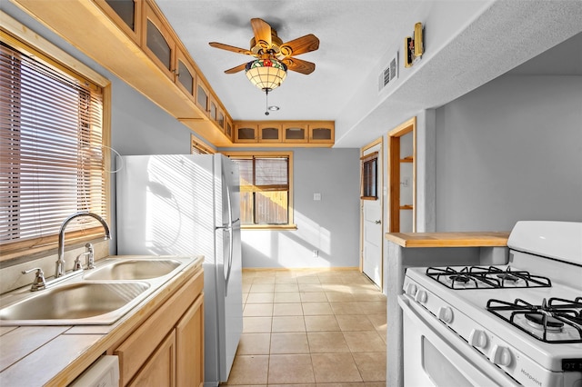 kitchen with sink, white appliances, light tile patterned floors, ceiling fan, and tile countertops