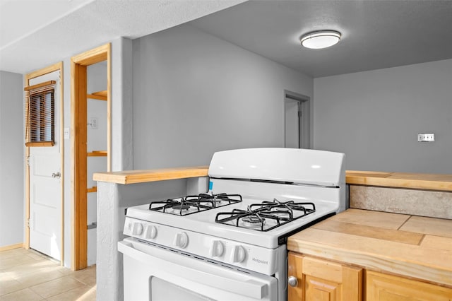 kitchen featuring white range with gas stovetop, light brown cabinets, and light tile patterned floors