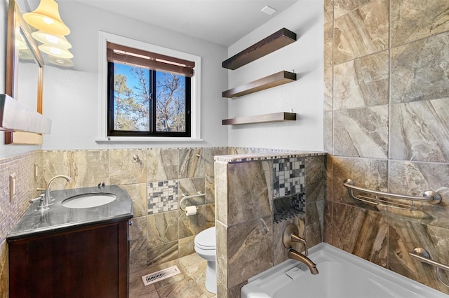 bathroom with vanity, a tub to relax in, tile walls, and toilet