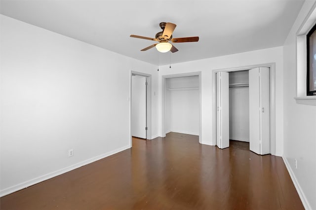 unfurnished bedroom with ceiling fan, dark hardwood / wood-style floors, and two closets