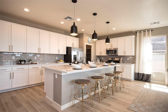 kitchen featuring an island with sink, white cabinetry, a breakfast bar area, hanging light fixtures, and stainless steel appliances